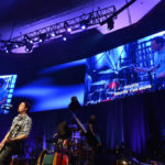 2 large digital displays behind stage with singer and band on stage